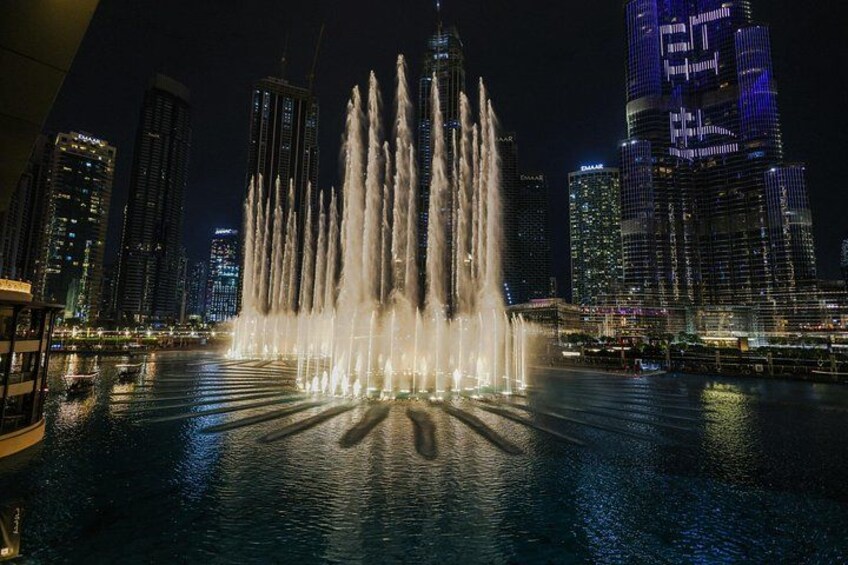 A nighttime cityscape with a prominent water fountain display in the foreground and illuminated skyscrapers in the background. 5