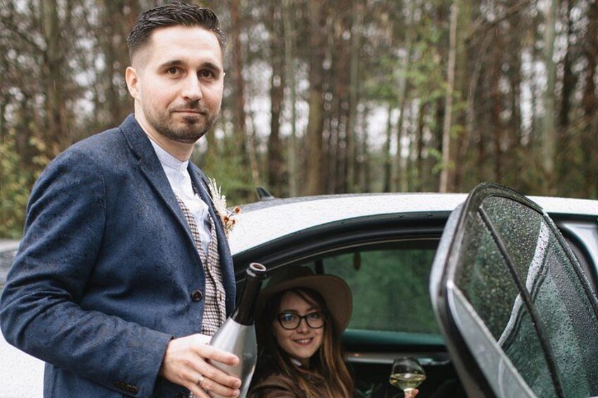 A man in a blue suit standing next to a car with a woman in the passenger seat. 3