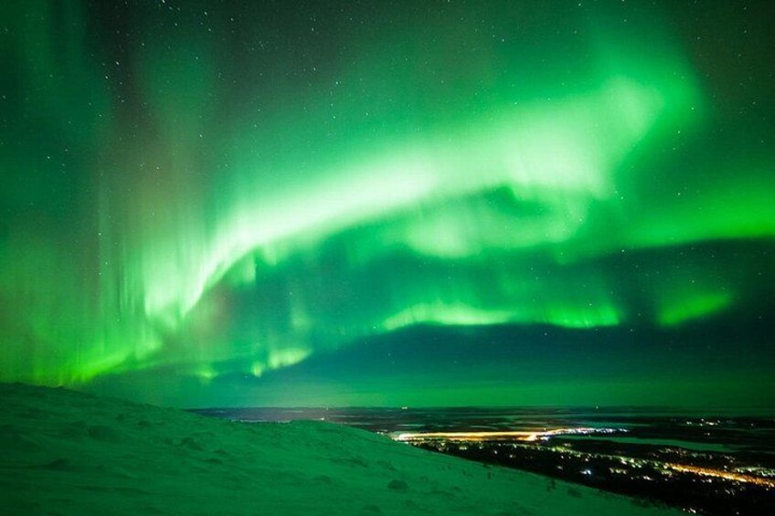 Nordlys over et snelandskab med en by i det fjerne. 2