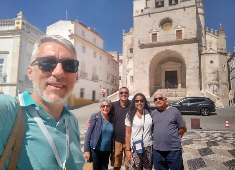 A group of people standing in front of a historic building with an arched entrance and a clock tower. 1