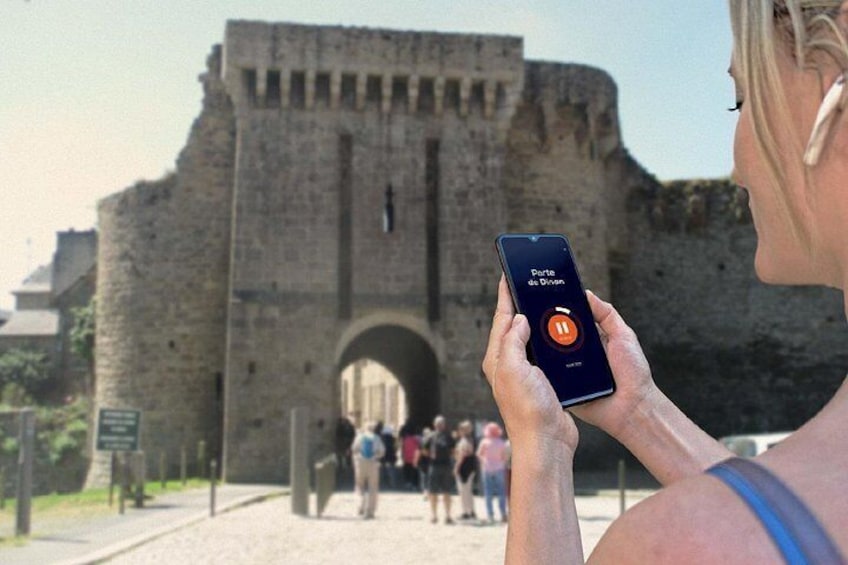 A person holding a smartphone with an app icon, standing in front of a historic stone archway. 5