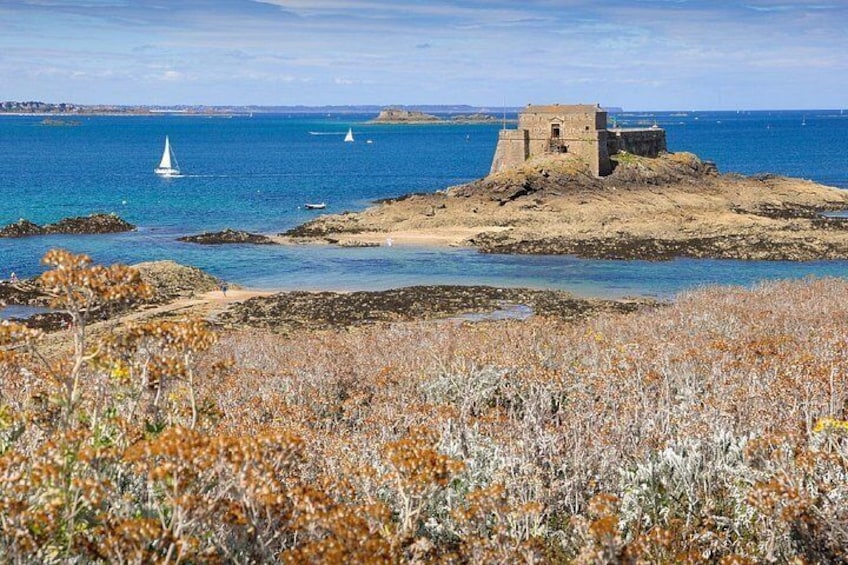 A coastal landscape with a rocky outcrop, a small building, and sailboats on the water. 2