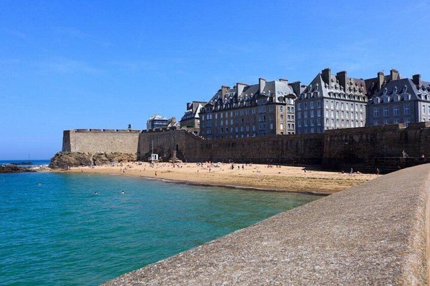 A coastal town with a historic fortification, a sandy beach, and a clear blue sea. 3