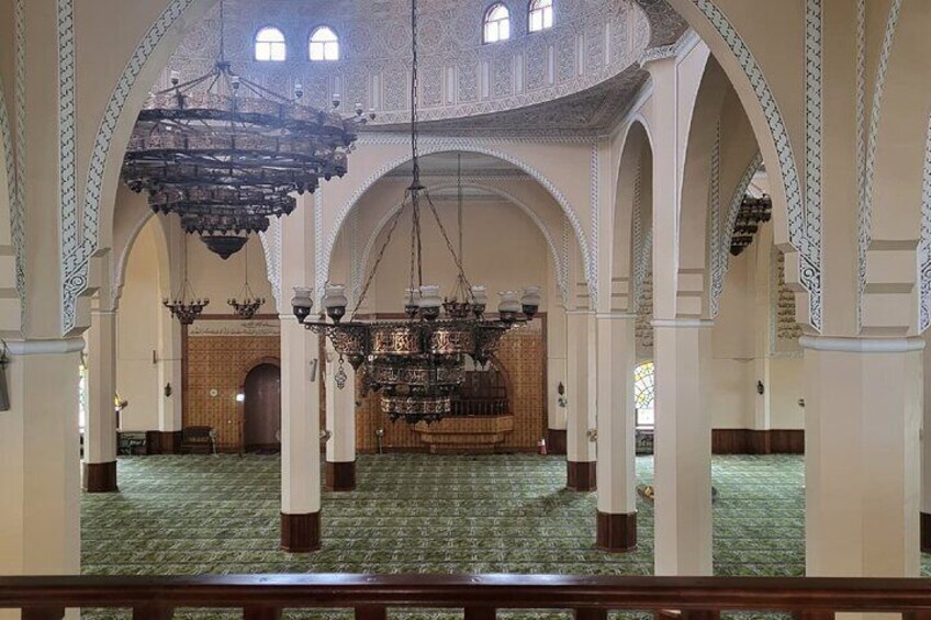An interior of a mosque with arches, chandeliers, and a prayer rug. 4