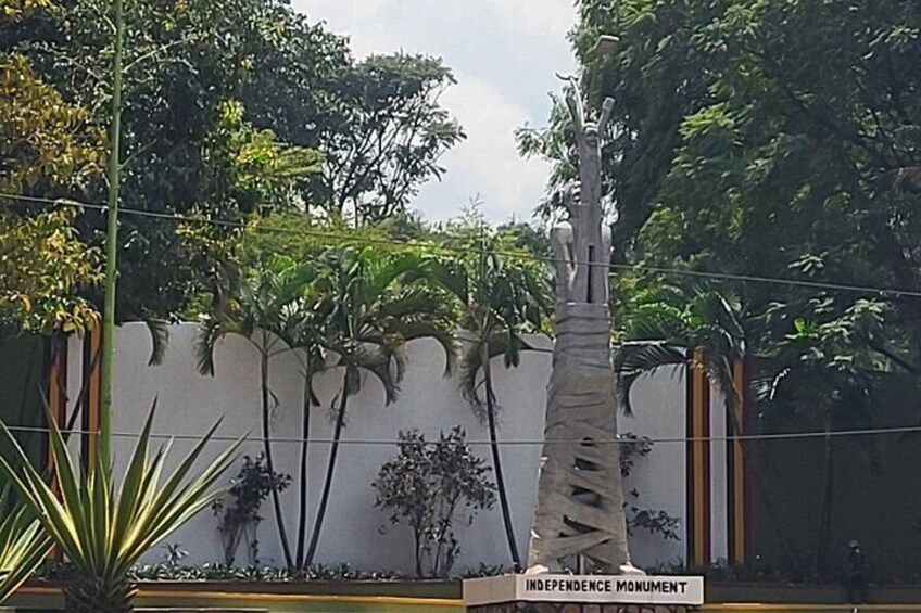 A statue of a man holding a flag, labeled 'Independence Monument', surrounded by tropical plants and trees. 5