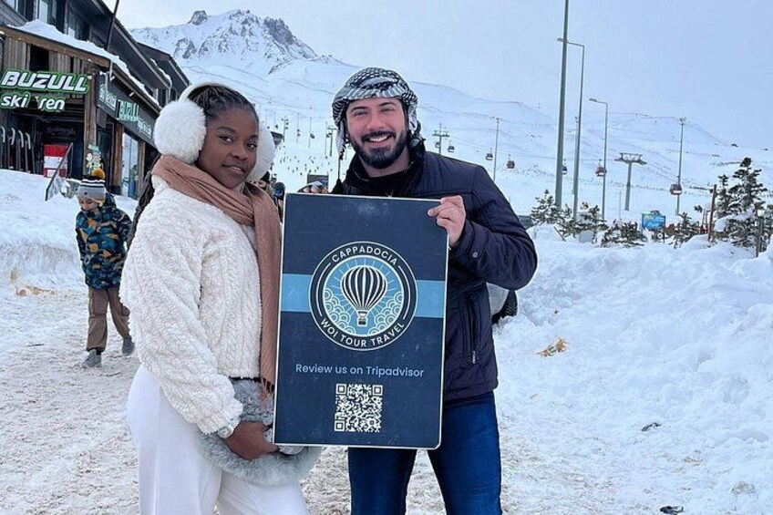 Dos personas sosteniendo un cartel con un código QR, situadas en una zona nevada con un telesilla y una montaña al fondo. 5