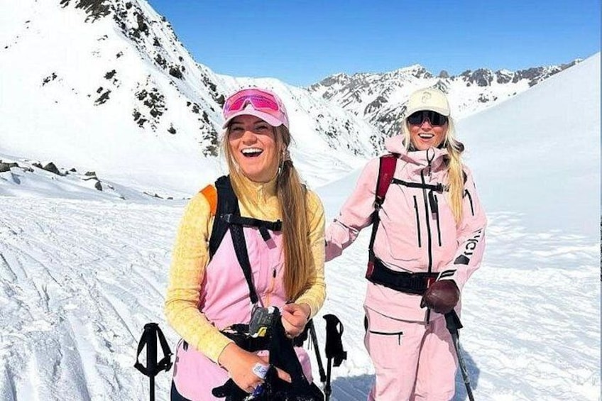 Dos personas con equipo de esquí rosa sobre una montaña nevada con cielo despejado. 4