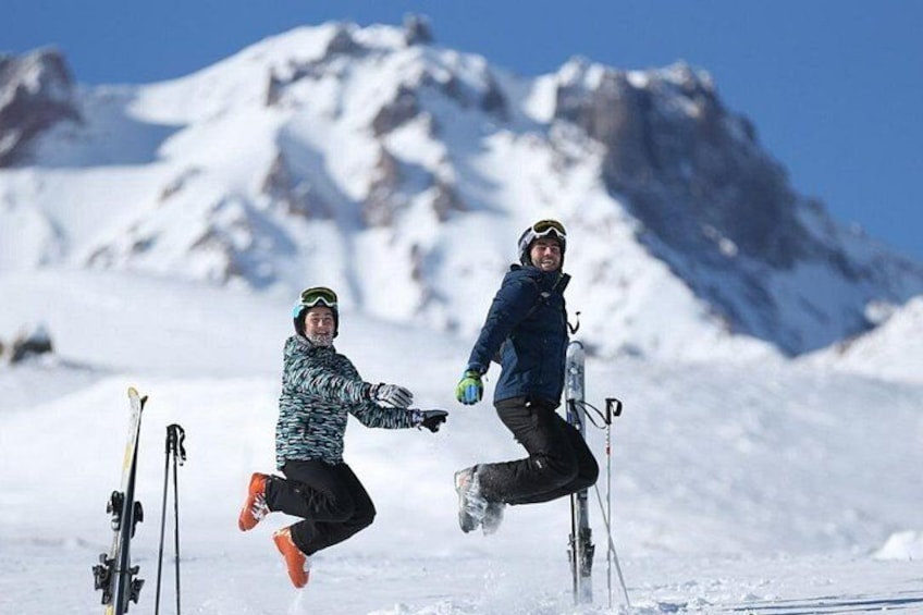 Dos personas esquiando en una ladera nevada, con esquíes y bastones, y una montaña al fondo. 1