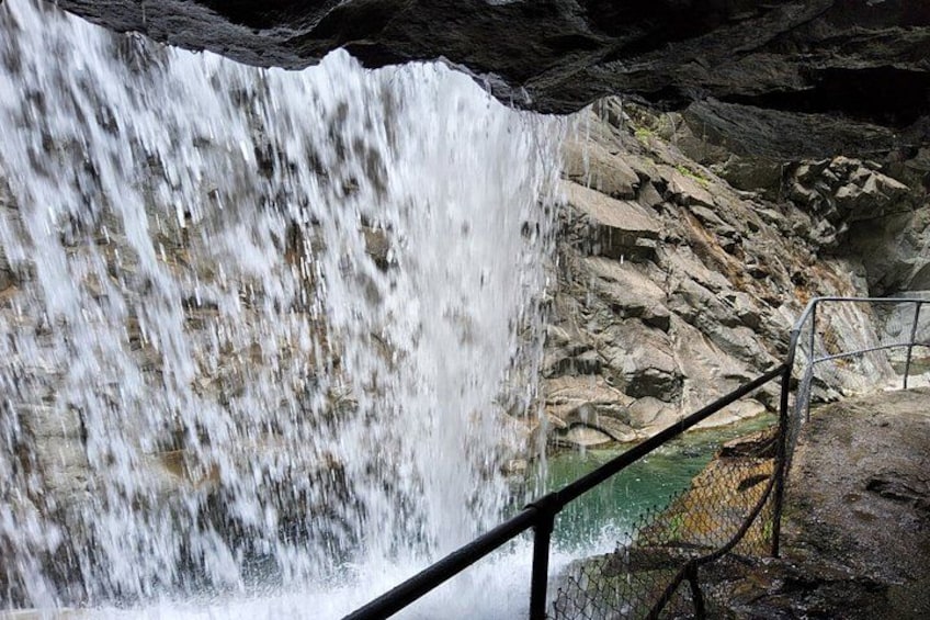 A waterfall cascading over rocks, a metal railing, and a pool of water at the base. 5