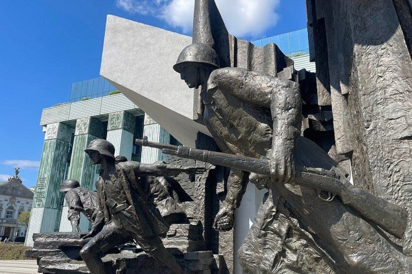 Eine Skulptur eines Soldaten mit Gewehr vor einem modernen Gebäude mit grünen Säulen. 3