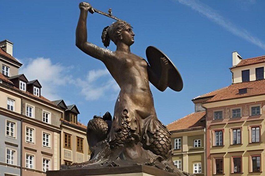 Eine bronzene Statue einer geflügelten Figur mit Speer vor einer Kulisse historischer Gebäude. 2