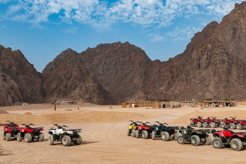 Paisaje desértico con montañas rocosas al fondo y varios cuatrimotos estacionados al frente. 3