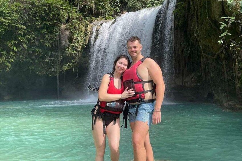 Two people standing in a body of water with a waterfall in the background. 2