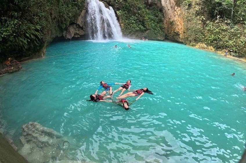 A group of people floating in a turquoise pool with a waterfall in the background. 4