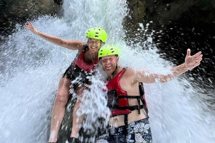 Two people in helmets and life vests near a waterfall. 1