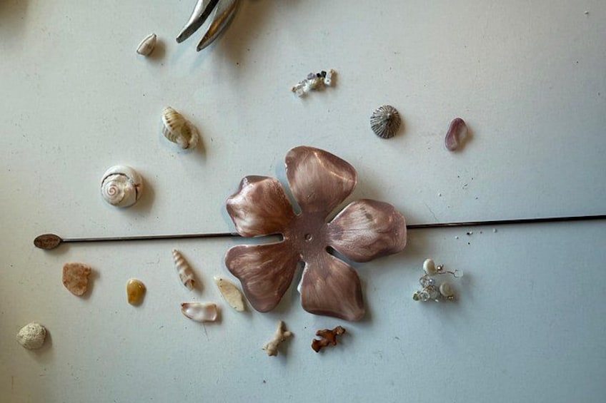 Ein blumenförmiges Objekt mit einer langen Stange, umgeben von verschiedenen Muscheln auf einer hellen Oberfläche. 2