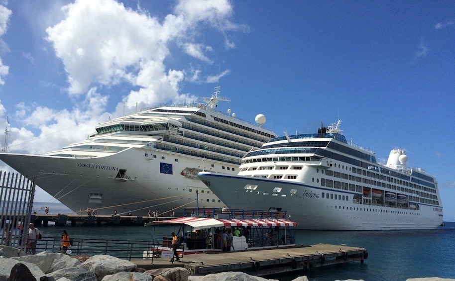 Dos grandes cruceros amarrados en un puerto con espigones rocosos y un cielo azul despejado. 2