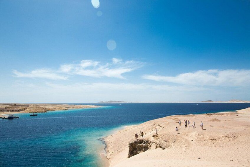 A coastal landscape with a clear sky, a sandy beach, and a few people walking along the shore. 2