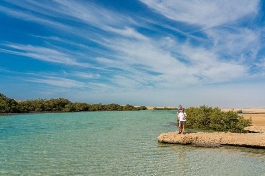 A person standing on a small island in a body of water with clear skies. 5