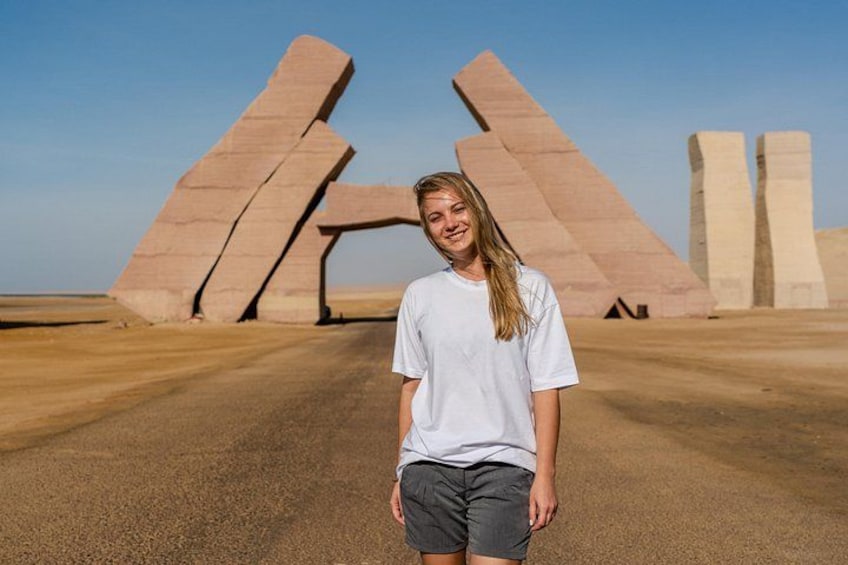 A person standing in front of large, angular stone structures in a desert landscape. 3