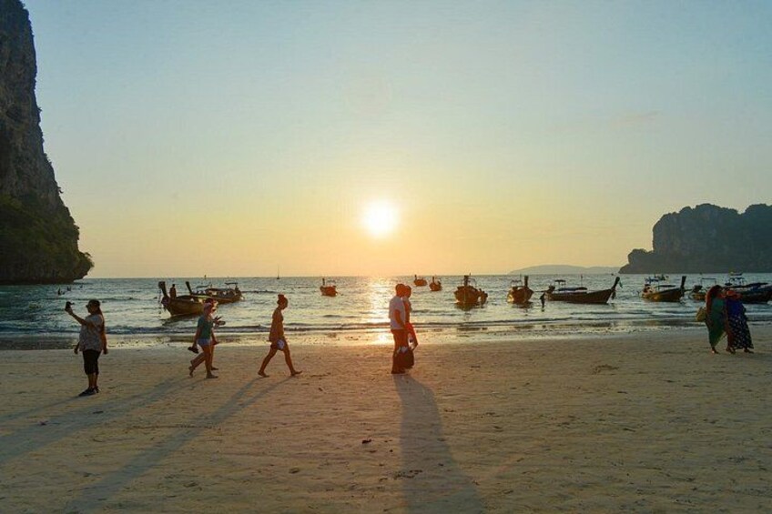 A beach with people walking, boats on the water, and a cliff in the background. 2