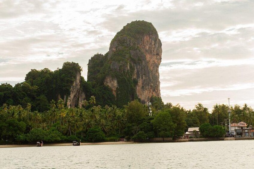 A large limestone karst mountain, palm trees, a body of water, and a few buildings. 3