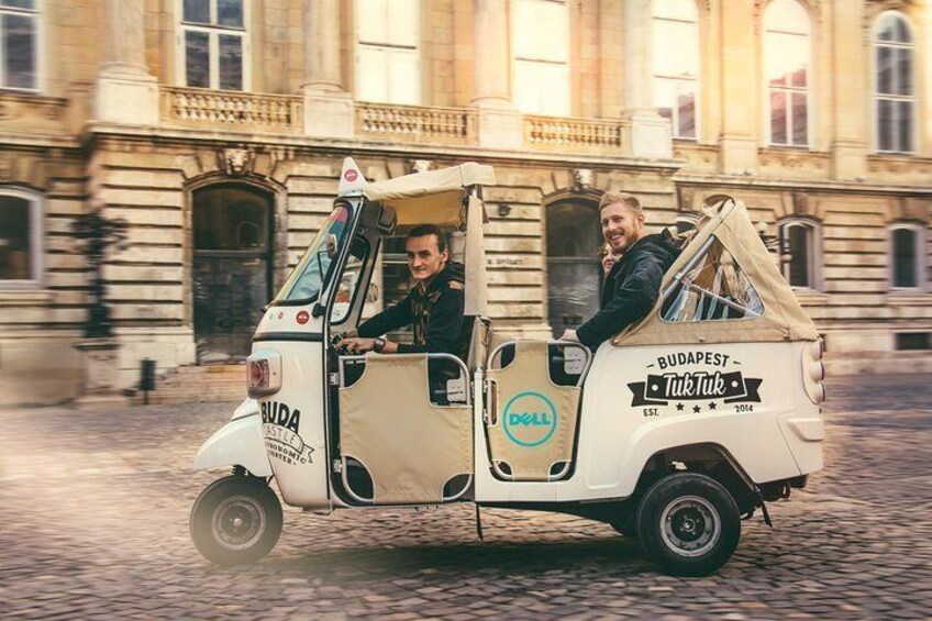 Een witte tuk-tuk met 'Budapest' en 'Tiktuk' aanduiding geparkeerd op een geplaveid straat. 3