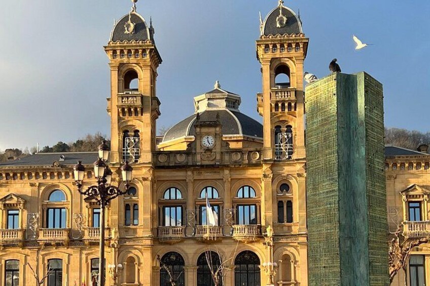 A historic building with two towers, a clock, and a modern glass building in the foreground. 1