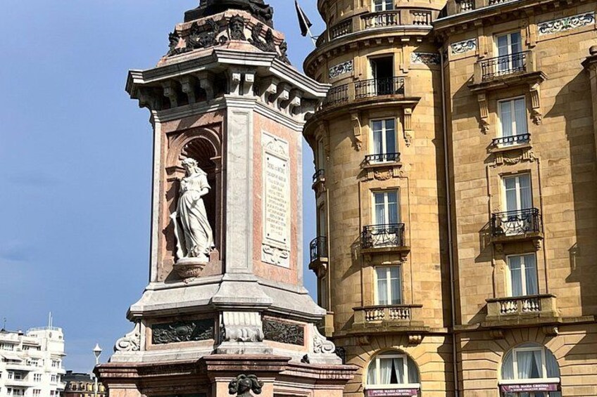 A classical statue on a pedestal, a corner building with balconies, and another building in the background. 4