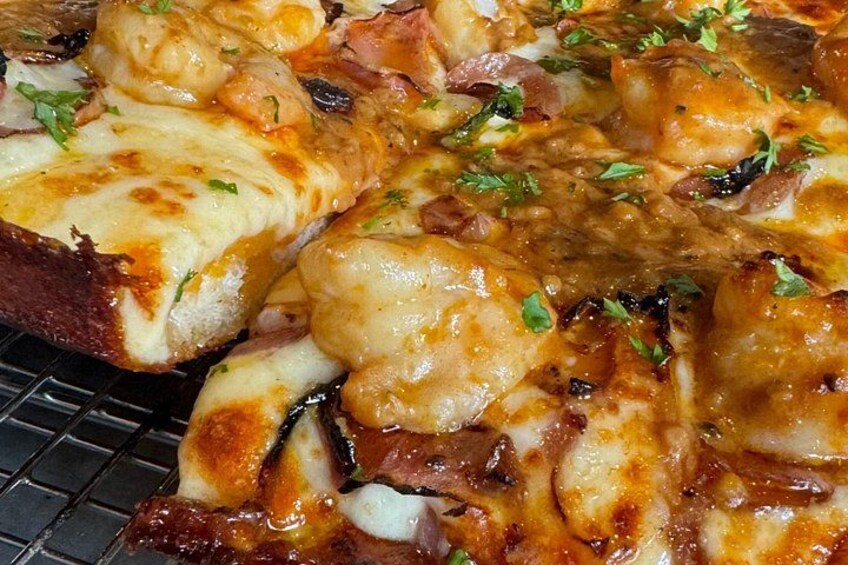 Primer plano de una pizza con queso derretido, jamón y hierbas. 3