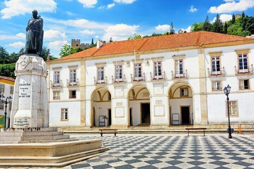 A historic building with a tiled roof, a statue in front, and a checkered pavement. 4