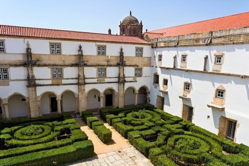 A historic building with a courtyard, arched walkways, and manicured hedges. 2