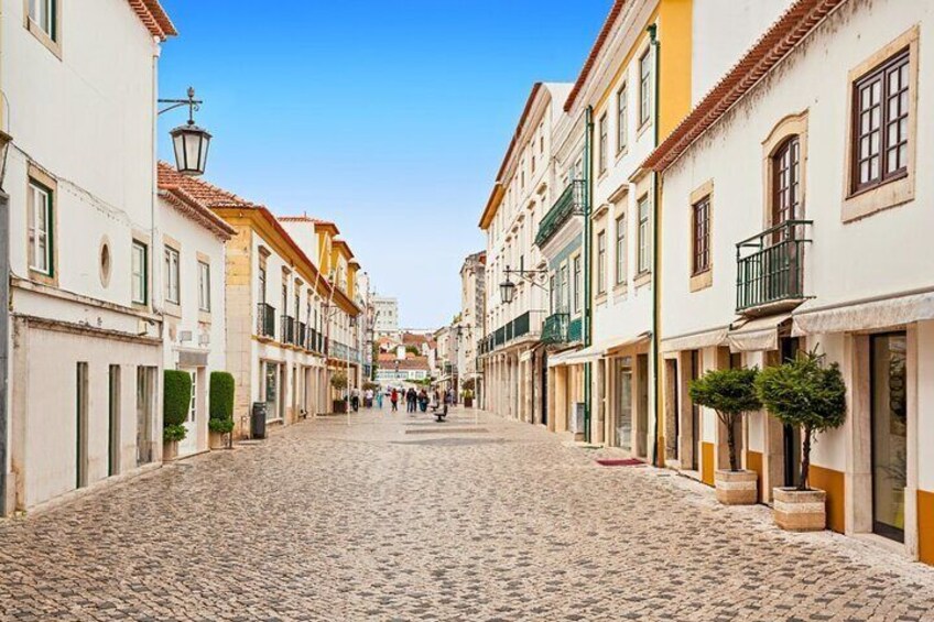A cobblestone street lined with historic buildings, a clear blue sky, and a few pedestrians. 3
