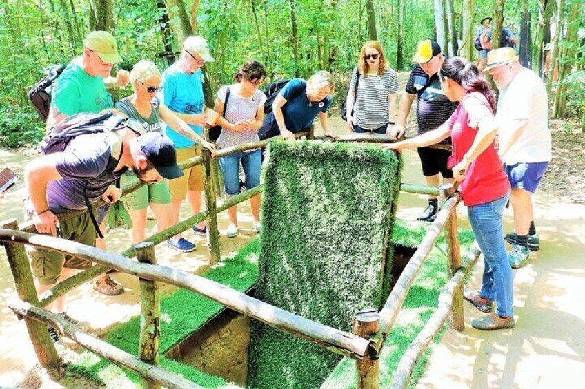 A group of people standing on a wooden bridge with a green artificial grass barrier, surrounded by a forested area. 4