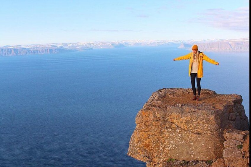 A person standing on a rocky outcrop with arms outstretched, overlooking a vast body of water and distant land. 1