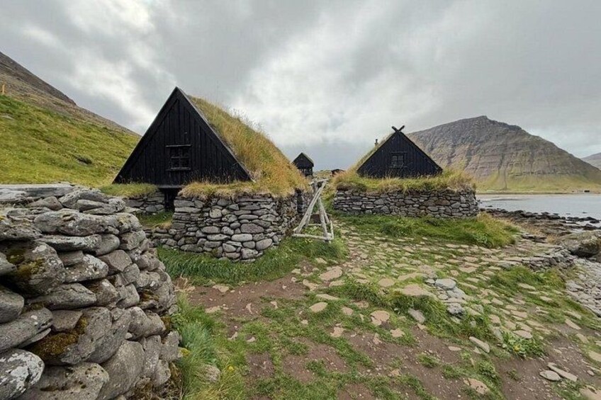 Traditional black houses with grass roofs, stone walls, and a rocky shoreline. 3