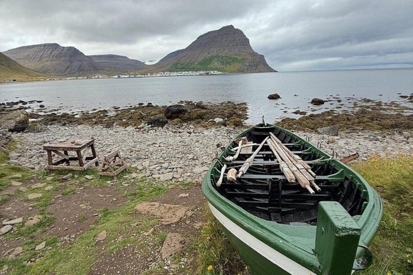 A green boat with wooden paddles on a rocky shore, a picnic table, and a mountainous landscape in the background. 4