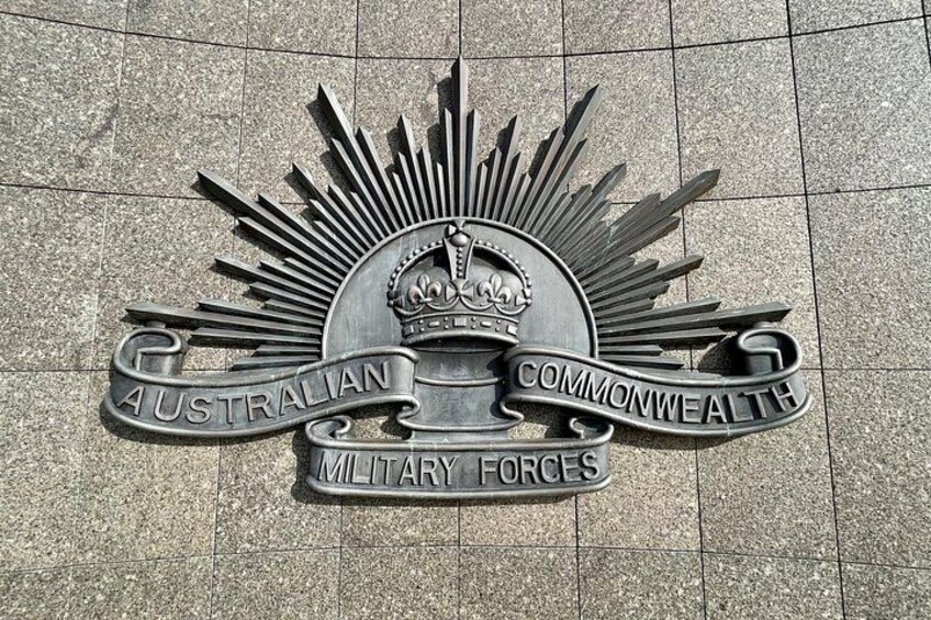 Ett metalliskt emblem med texten ”Australian Commonwealth Military Forces” på en stenyta. 3