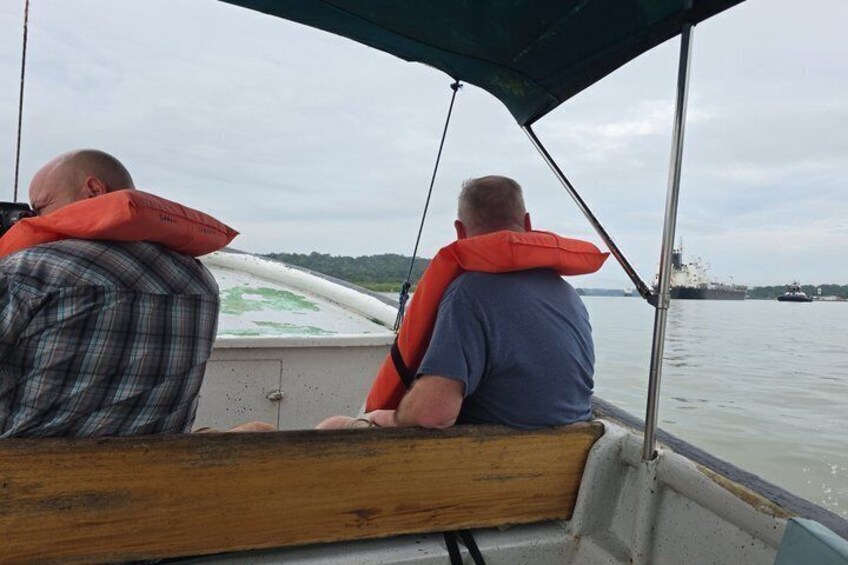 Dos personas en un bote con chalecos salvavidas, con un río y barcos a lo lejos. 4