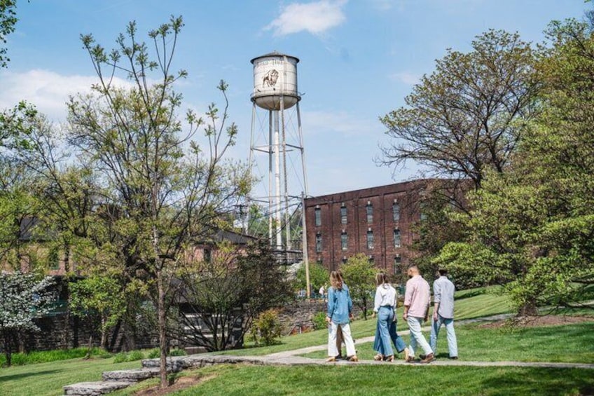 A group of people walking on a grassy path, a water tower, and a brick building in the background. 2