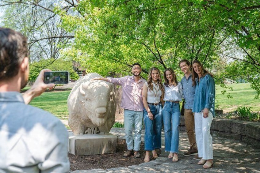 A group of people standing under a tree with a stone sculpture in a park. 4