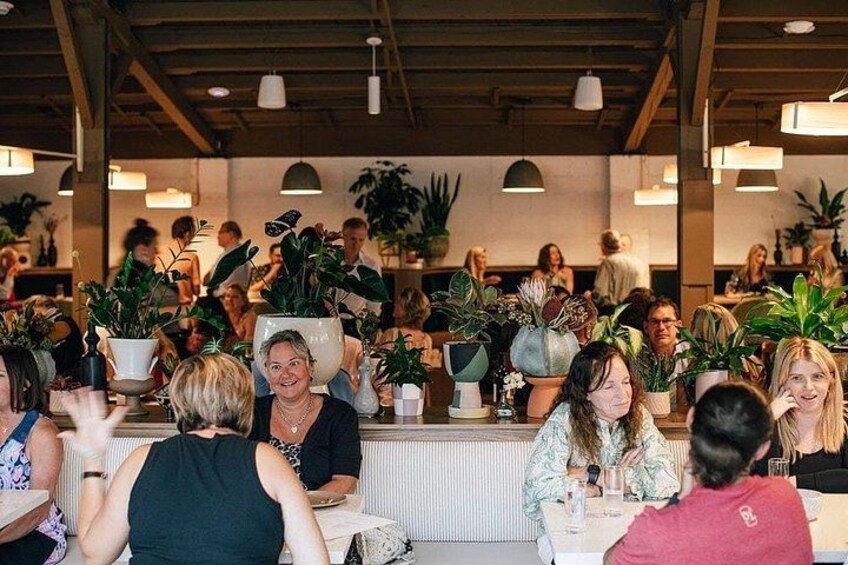 A restaurant interior with patrons seated at tables, surrounded by potted plants. 3