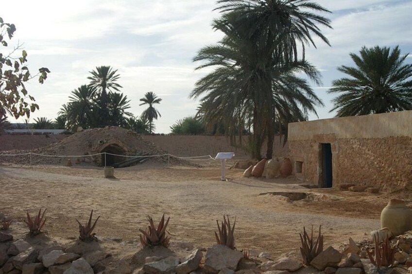 A desert landscape with a small mound, palm trees, and a building with a doorway. 4