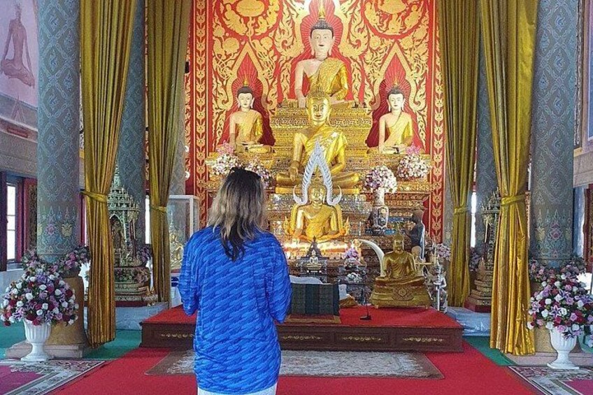 A person in a blue garment standing in front of a large Buddha statue in a temple. 5