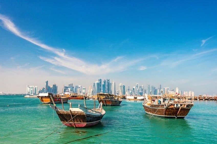 Traditional wooden boats docked in clear turquoise water with a modern city skyline in the background. 5