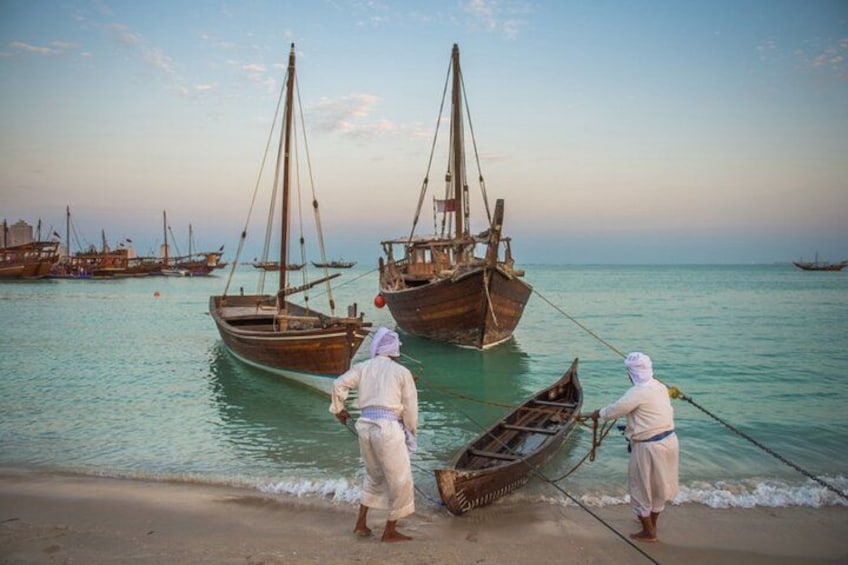 Two people pulling a boat onto a sandy beach with several other boats in the background. 4