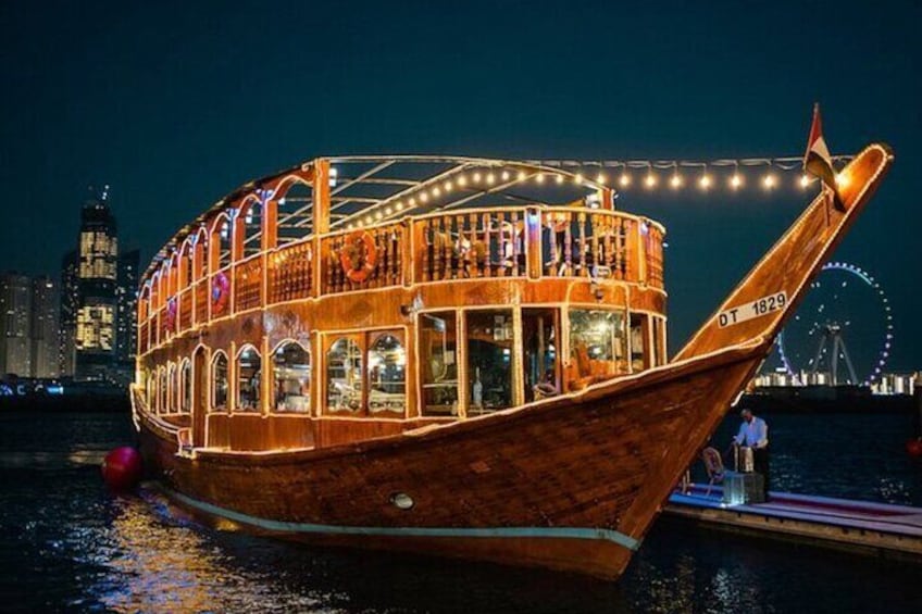 Una barca de madera con luces, amarrada en un muelle con un horizonte urbano y una noria al fondo. 2