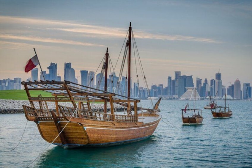 A wooden boat with a flag, docked near a city skyline. 3