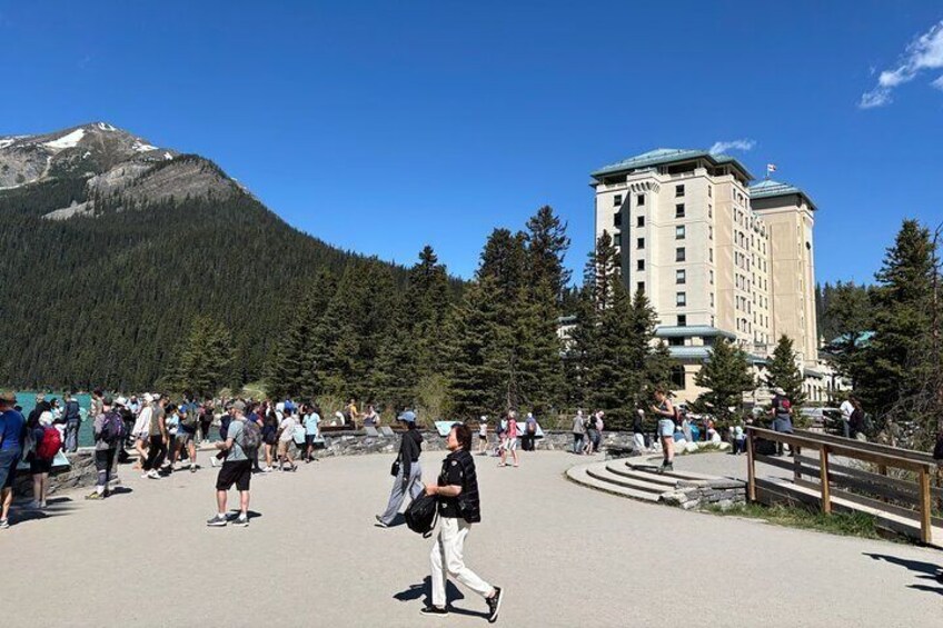 Paesaggio montuoso con un grande edificio, un vialetto lastricato e persone che passeggiano. 4