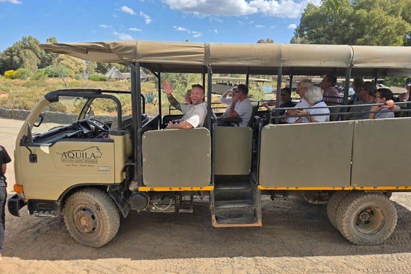 A safari vehicle with passengers, a desert landscape, and sparse vegetation. 1